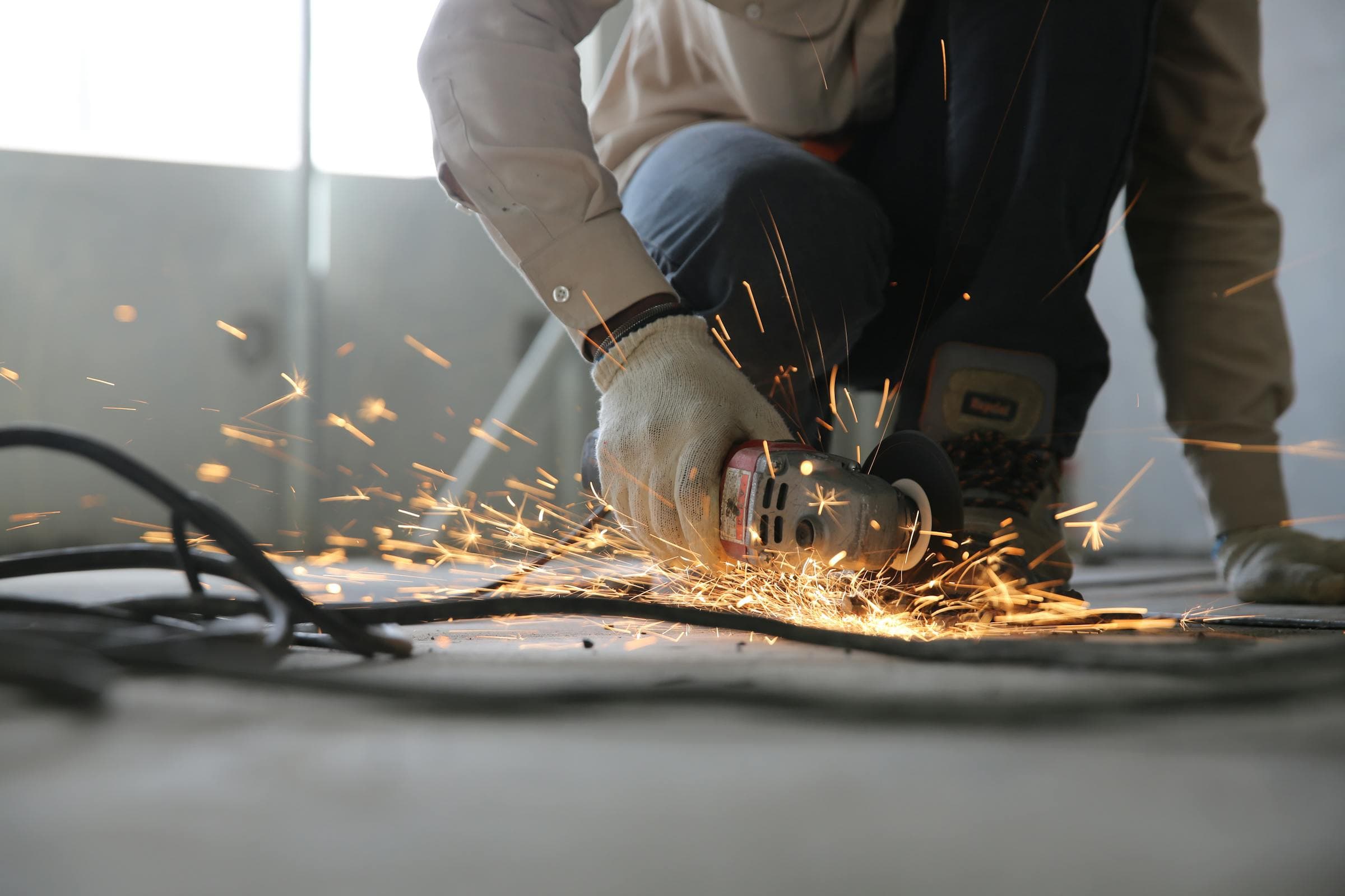 Worker wearing cotton knit glove using an angle grinder with sparks flying